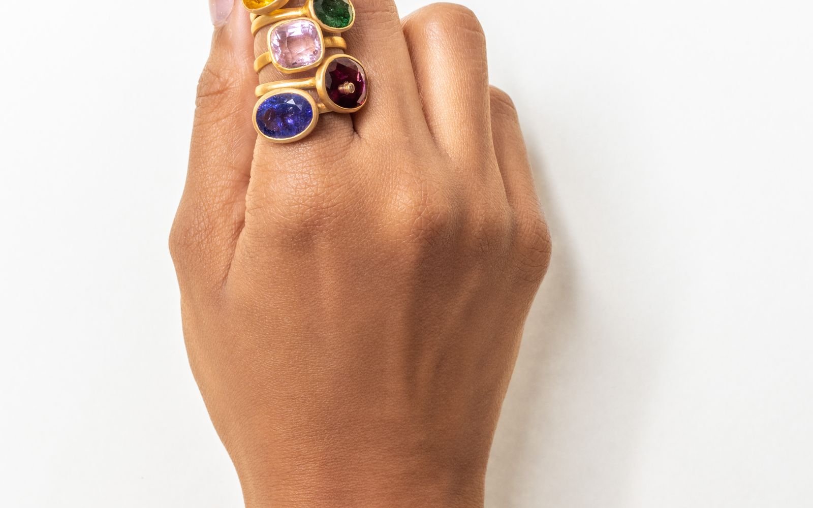Colourful gemstone rings on hand with gold bracelet